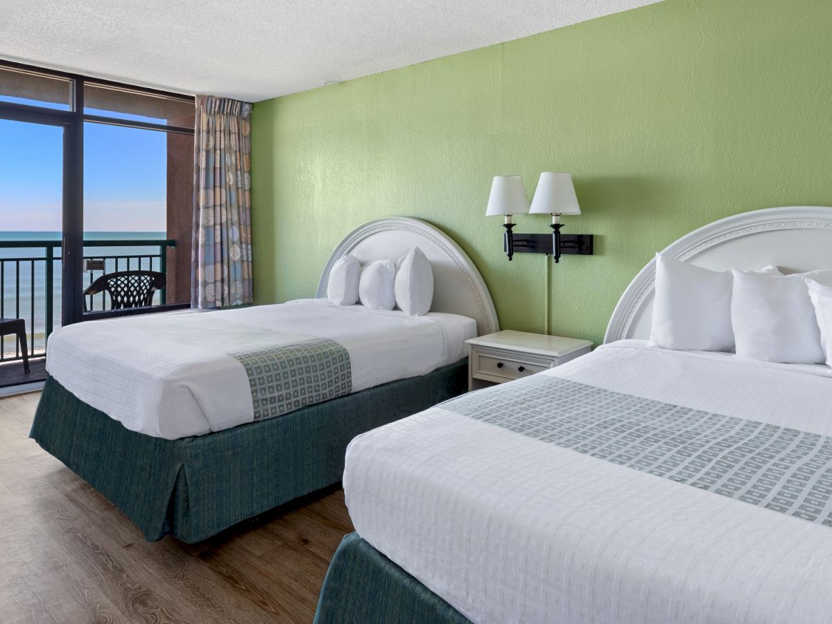 The image shows a hotel room with two large beds, green walls, and a balcony with a view of the ocean outside.