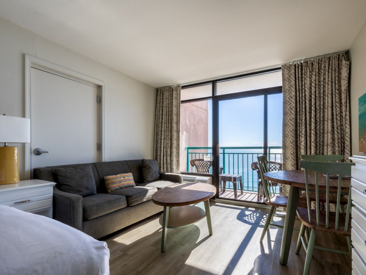 A cozy living area with a sofa, table, chairs, and a balcony with an ocean view; the room has a modern and clean design, offering relaxation.