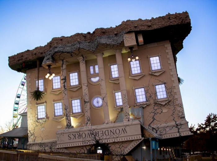 This image shows an upside-down building with the sign "WonderWorks" on it, featuring cracked walls and a Ferris wheel visible in the background.