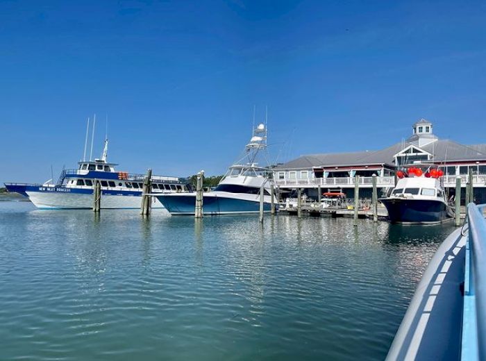 The image shows boats docked at a marina with a nearby building under a clear blue sky, reflecting a tranquil waterfront setting.