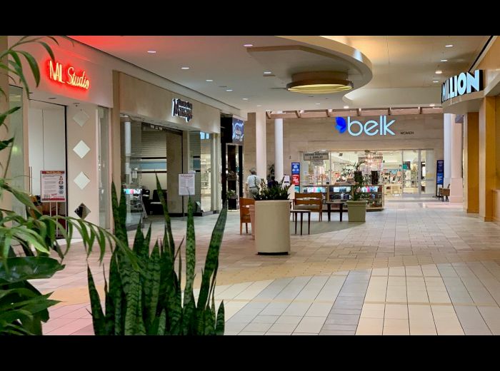 The image shows a shopping mall corridor with various storefronts, including Belk and Hibbett Sports, with plants and seating areas in the center.