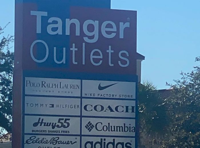 A sign for Tanger Outlets listing several stores, including Nike, Coach, Columbia, Tommy Hilfiger, Adidas, Eddie Bauer, Hurley, and Polo Ralph Lauren.