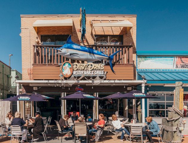 People are dining outdoors at a restaurant named Duffy's Oar House. The building has a large marlin statue mounted on the balcony.