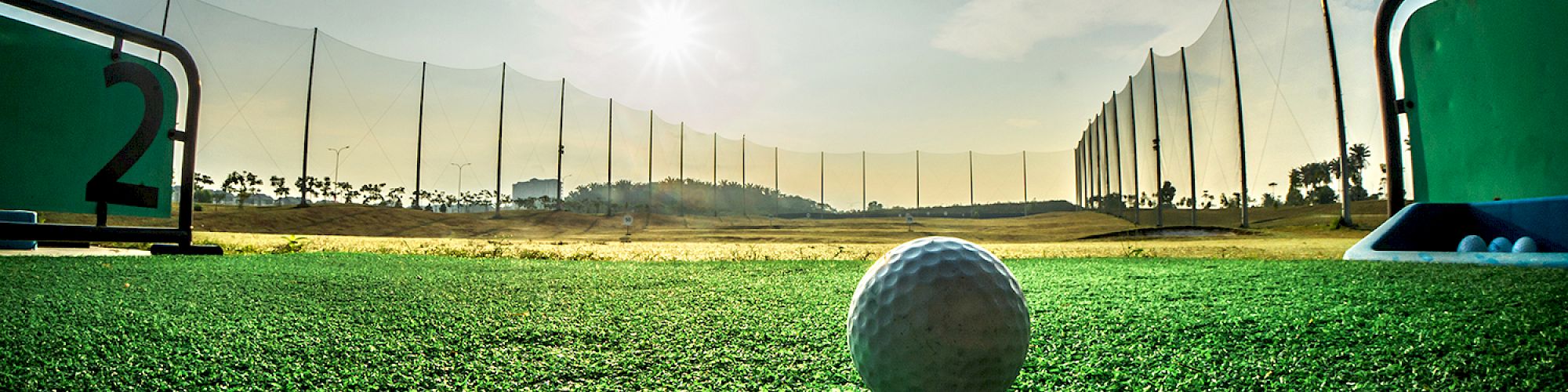 A close-up of a golf ball on a driving range mat, with a sunny sky and practice nets in the background, creating a serene golfing atmosphere.