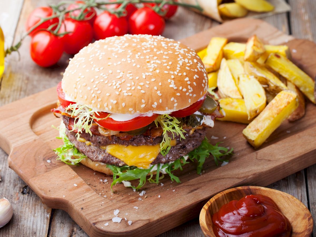The image features a delicious cheeseburger with lettuce and tomato on a wooden board, accompanied by thick-cut fries, ketchup, and mustard dip.